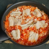 Перемешиваем томатный соус с рисом, солим и выкладываем сверху припущенное филе минтая