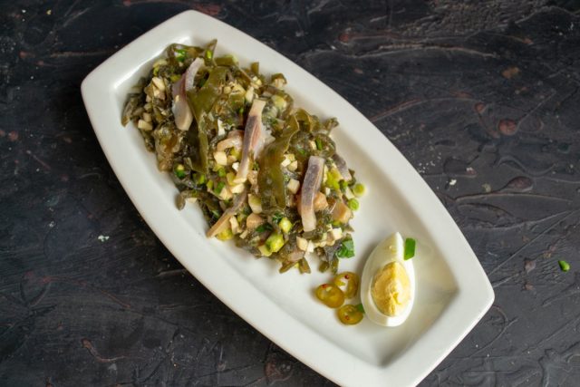 Выкладываем салат на овальную тарелку, рядом кладём ломтик варёного яйца и маринованный чили